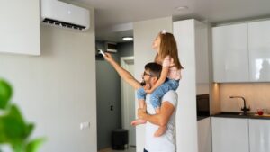A man carries a girl on his shoulders as she uses a remote control to operate an air conditioner in a modern kitchen. AC Repair Anderson